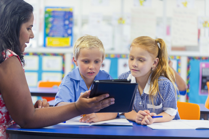 Aboriginal school teacher using digital tablet. She is talking and showing the children something on the computer in the classroom