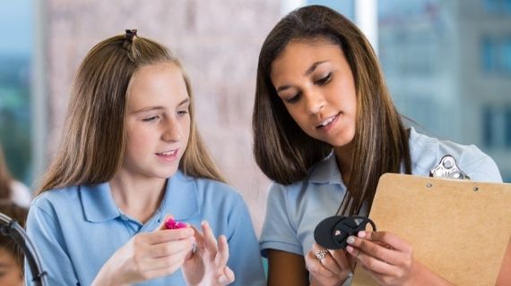 two students comparing objects in classroom